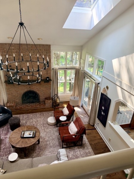 Living room with a brick fireplace, terracotta leather chairs, and a round wood coffee table beneath a black iron chandelier