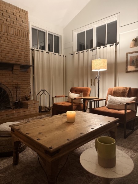 Living room in the evening with a brick fireplace, terracotta chairs, and a candlelit wood coffee table