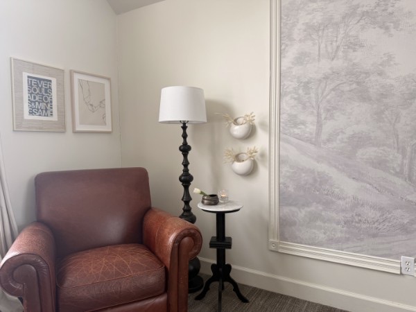 Reading nook with a worn leather club chair, black floor lamp, and landscape mural